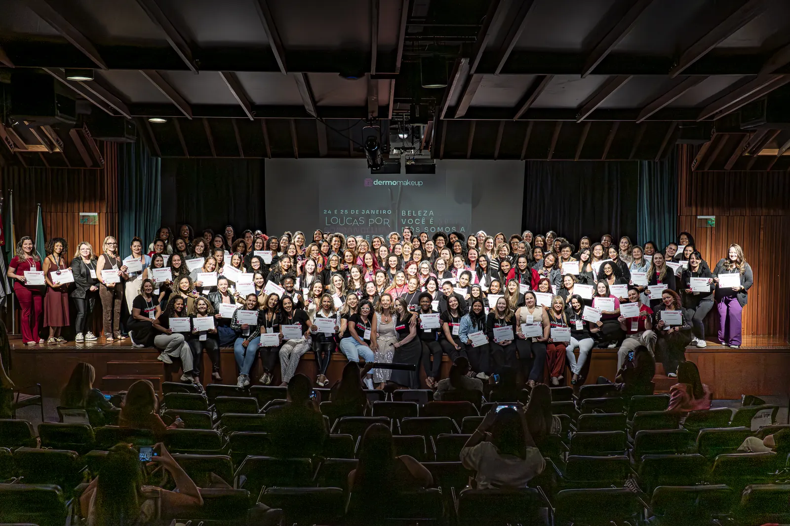 Auditório lotado do LoUcAs 2026 com todas as participantes no palco